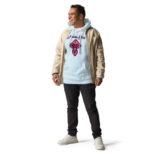 A man stands against a white background, wearing a tan jacket over the Unisex Mama Dose Mushroom Hoodie, black jeans, and white sneakers, smiling.