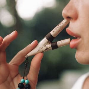 Person playing a small woodwind instrument with two pipes near their lips, adorned with beads.