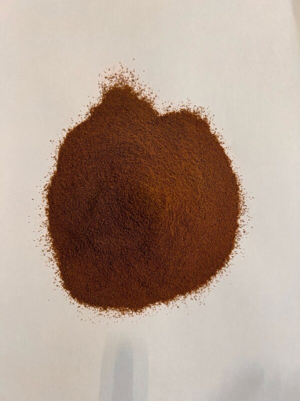 A pile of finely ground brown Mama's Functional Mushrooms Instant Coffee is spread on a white surface.