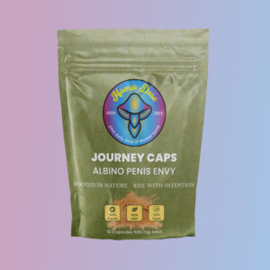 A green resealable pouch labeled “Journey Caps ALBINO PENIS ENVY (APE) strain” by Aroma Dose, containing 10 vegan mushroom capsules, appears against a pink and blue gradient background.