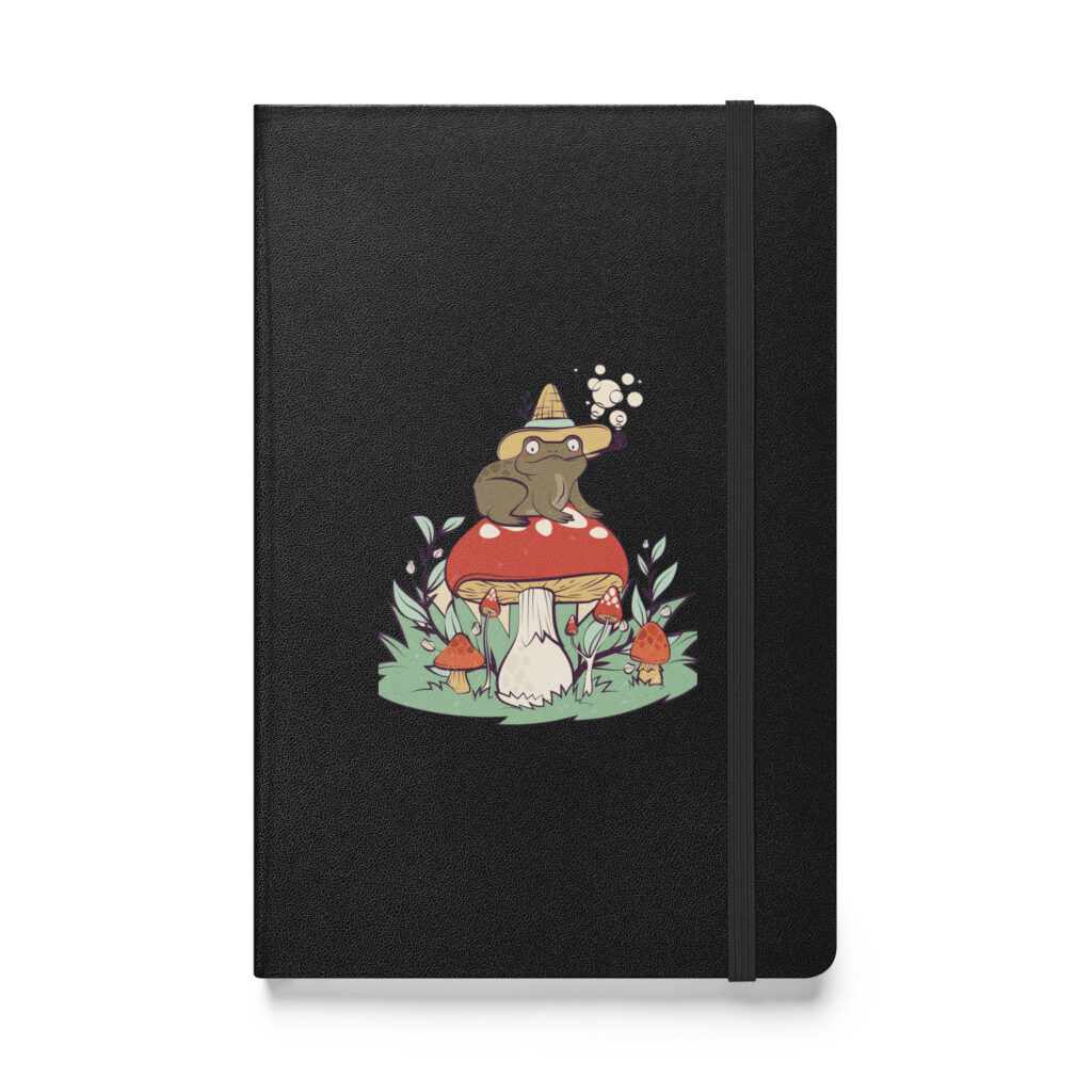 The Forest Observer hardcover notebook features a black cover with an illustration of a frog in a hat and glasses, sitting on a red mushroom amid grass and smaller mushrooms.