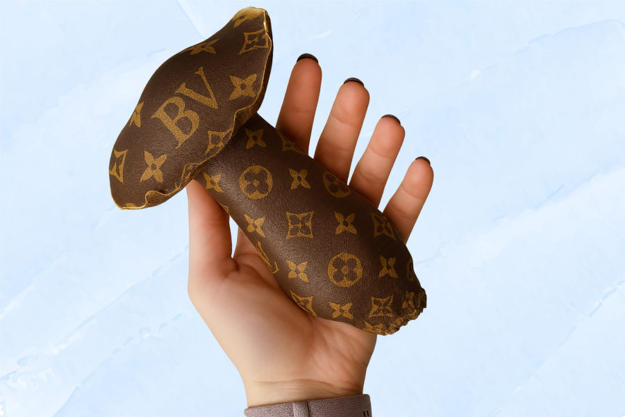 A hand holding a Bluey Vuitton mushroom with a distinctive brown cap featuring a luxurious Louis Vuitton-inspired pattern, including "BV" logos, against a light blue background.