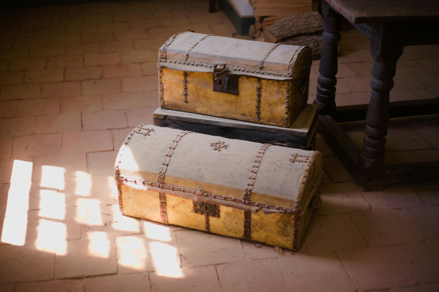 Two vintage wooden trunks with metal locks stacked on a terracotta tile floor in soft window light, symbolizing safe storage and stewardship