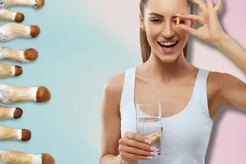 A woman smiles, holding a yellow capsule and a glass of water, while mushrooms rest neatly on the left side against a pastel background, alluding to the practice of microdosing magic mushrooms.