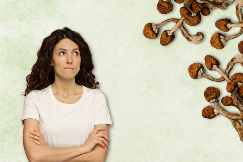 A woman with arms crossed looks up thoughtfully, pondering what are psilocybin mushrooms, while dried mushrooms are arranged in the upper right corner against a light background.