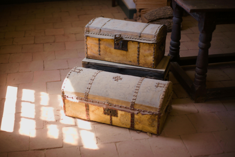 Two vintage wooden trunks with metal locks stacked on a terracotta tile floor in soft window light, symbolizing safe storage and stewardship